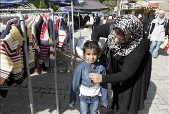 عراقية تتسوق لطفلتها استعداداً لعيد الأضحى في الكرادة في بغداد أمس