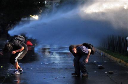 طالبان يحتميان من مدفع مياه الشرطة خلال الاشتباكات في سانتياغو امس (ا ب ا) 