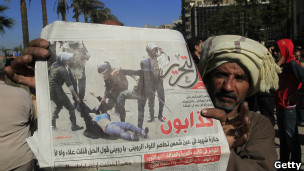 متظاهر يحمل صحيفة تعرض صوة ضرب قوات الجيش لفتاة منزوعة الملابس