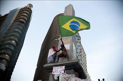 متظاهر برازيلي يلوح بعلم بلاده من على مبنى خلال الاحتجاجات في مدينة بيلو هوريزونتي أمس الأول (أ ف ب) 