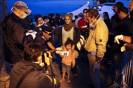عنصر من الشرطة الايطالية يلتقط صورة لطفلة وصلت ضمن مجموعة من اللاجئين السوريين والفلسطينيين الى صقلية امس (رويترز) 