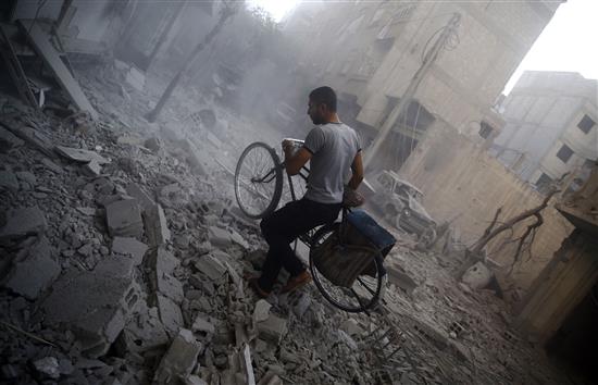 شاب يمر بدراجته الهوائية بين ركام مبنى تعرض الى غارة جوية في دوما في ريف دمشق امس (ا ف ب)