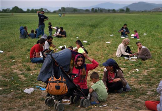 لاجئون يجلسون على العشب قرب الحدود المقدونية-اليونانية امس (ا ف ب)